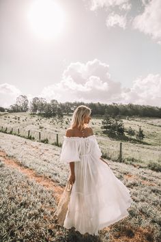 a woman in a white dress walking down a dirt road