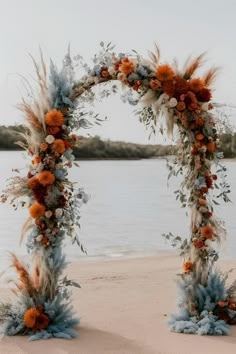 an orange and blue wedding arch on the beach with pamolite, flowers and feathers