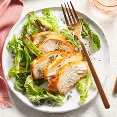 a white plate topped with meat and lettuce next to a knife and fork