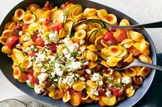 a bowl filled with pasta and vegetables on top of a white table next to a spoon