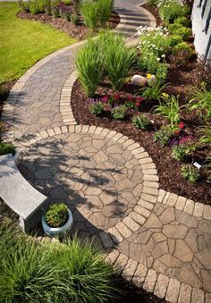 a stone path leading to a house with flowers in the foreground and a bench on the other side