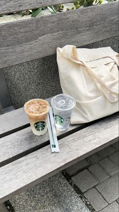 two cups of coffee sitting on top of a wooden bench next to a white bag