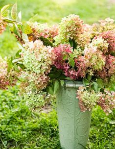 a green vase filled with lots of flowers on top of a lush green field next to grass