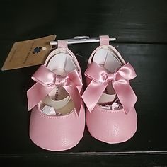 a pair of pink baby shoes with a bow on the front and bottom, sitting on a black surface