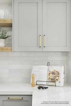 an open book on a counter in a kitchen with white cabinets and gold handles,