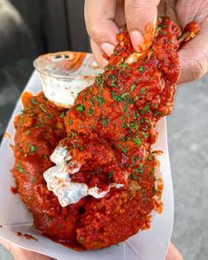 a person holding up a piece of food with sauce on it