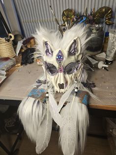 a white mask with feathers and jewels on top of a wooden table next to other items