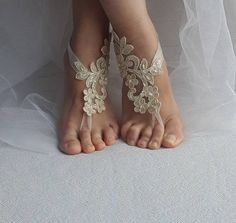 the barefoot bride's feet are adorned with white lace and flowers, while her veil is draped over them