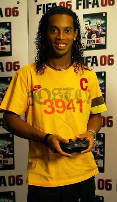 a young man holding a game controller in his hand and smiling at the camera while wearing a yellow shirt