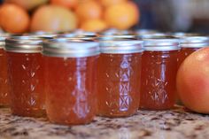 several jars filled with liquid sitting on top of a counter next to oranges and an apple