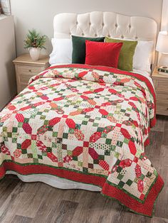 a bed with a red and green quilt on it's headboard next to a night stand