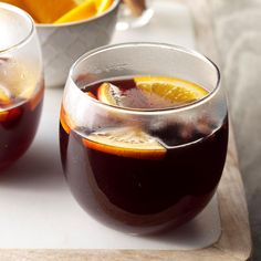 two glasses filled with liquid sitting on top of a cutting board next to orange slices