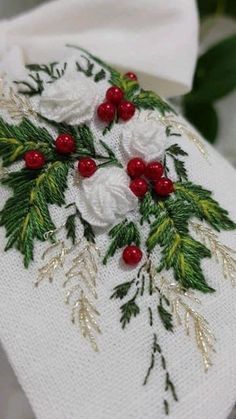 a white towel with red berries and green leaves on it, sitting next to some flowers