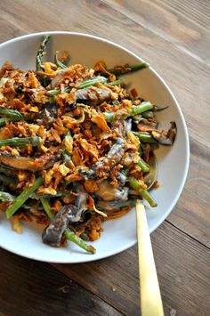 a white plate topped with green beans and mushrooms next to a yellow spoon on top of a wooden table