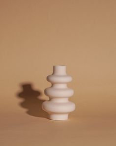 a white vase sitting on top of a table next to a shadow from the wall