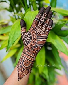 a woman's hand with henna tattoos on it and green leaves in the background