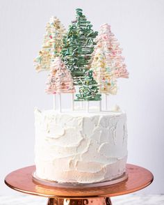 a white cake topped with trees on top of a wooden table next to a gold plate