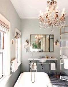 a white bath tub sitting under a chandelier next to a sink and mirror