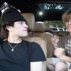 two young men sitting in the back seat of a car, one is talking to the other