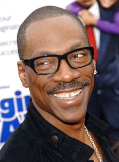 a man with glasses and a mustache smiles at the camera while standing in front of other men