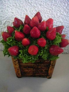 a wooden basket filled with lots of strawberries on top of a white table next to a wall