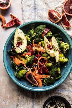 a blue bowl filled with broccoli, oranges and other food on top of a table