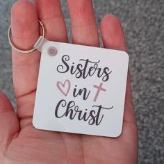 a hand holding a white keychain with the words sisters in christ on it