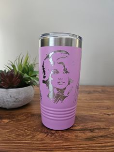 a pink tumbler cup with an image of a woman on it next to a succulent plant