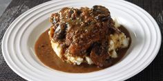 a white plate topped with meat and gravy covered in gravy on top of mashed potatoes