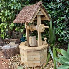 a wooden wishing well with a straw roof and water spigot on it's side