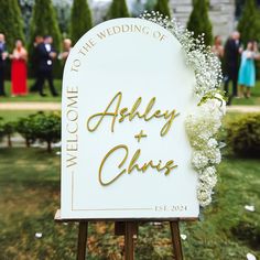 a welcome sign with flowers on it in the middle of a garden at a wedding