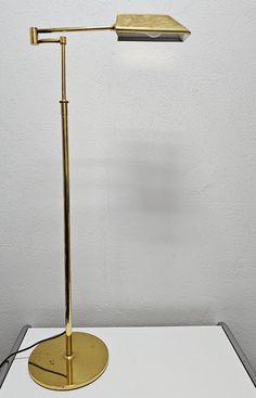 a gold desk lamp sitting on top of a white table next to a white wall