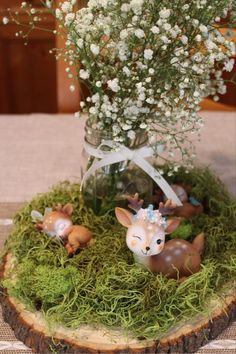 a vase filled with baby's breath flowers and deer figurines on top of moss