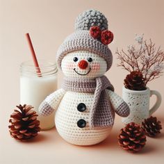 a crocheted snowman next to two pine cones and a glass of milk