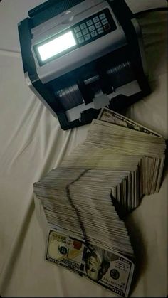 a pile of money sitting next to a printer on top of a white sheet covered bed