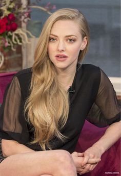 a woman with long blonde hair sitting on a purple couch and looking at the camera