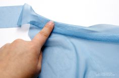 a person's hand is pulling up the blue fabric on a piece of cloth