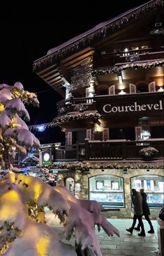 people are walking on the sidewalk in front of a building covered with snow at night