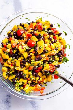 a glass bowl filled with black beans, corn and tomato salad on top of a white table