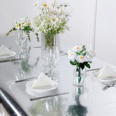 the table is set with white plates and flowers in glass vases on each side