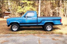 a blue pick up truck parked in front of some trees and grass with no leaves on the ground