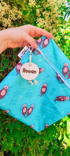 a hand holding a blue bag with pink birds on it and the name rowan written on it