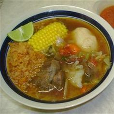 a bowl of soup with meat, rice and corn on the cob in it