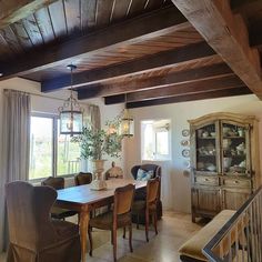 a dining room table and chairs in front of a window with wooden beams on the ceiling