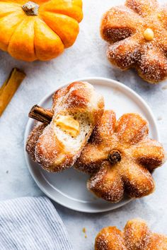 some sugared donuts are on a plate with cinnamon sticks and pumpkins in the background