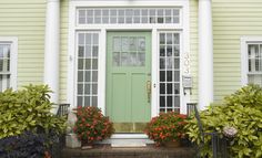 a green front door on a yellow house with potted plants and flowers around it