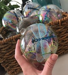 a hand holding a clear glass ball with dragon designs on it and some plants in the background