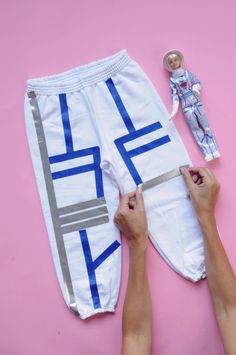 two hands are working on a pair of white sweatpants with blue and silver stripes