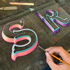 someone is painting the letters in pink, blue and green with scissors on the ground