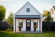 a small white house with two potted plants on the front porch and one door open